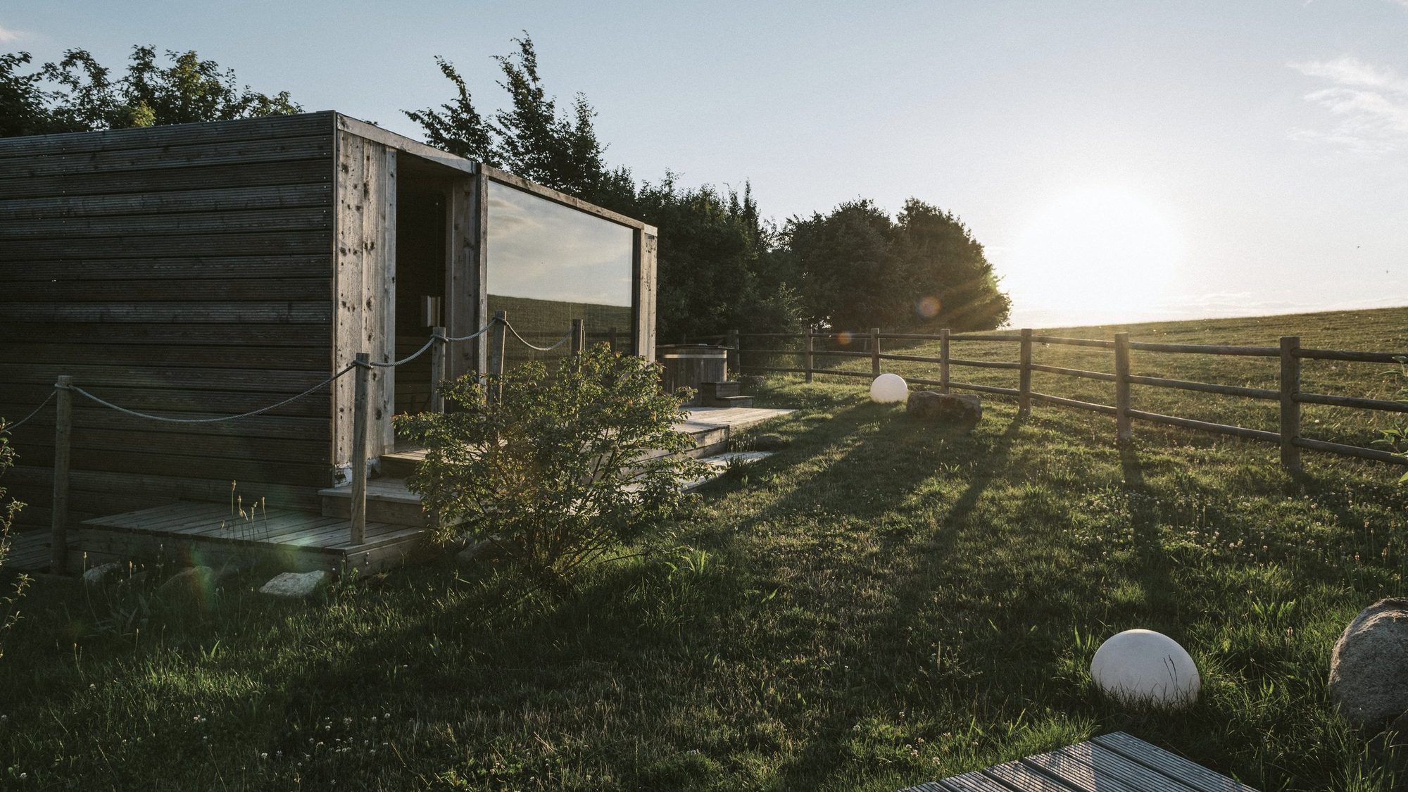 Venkovní sauna a koupací káď nad pastvinou při západu slunce